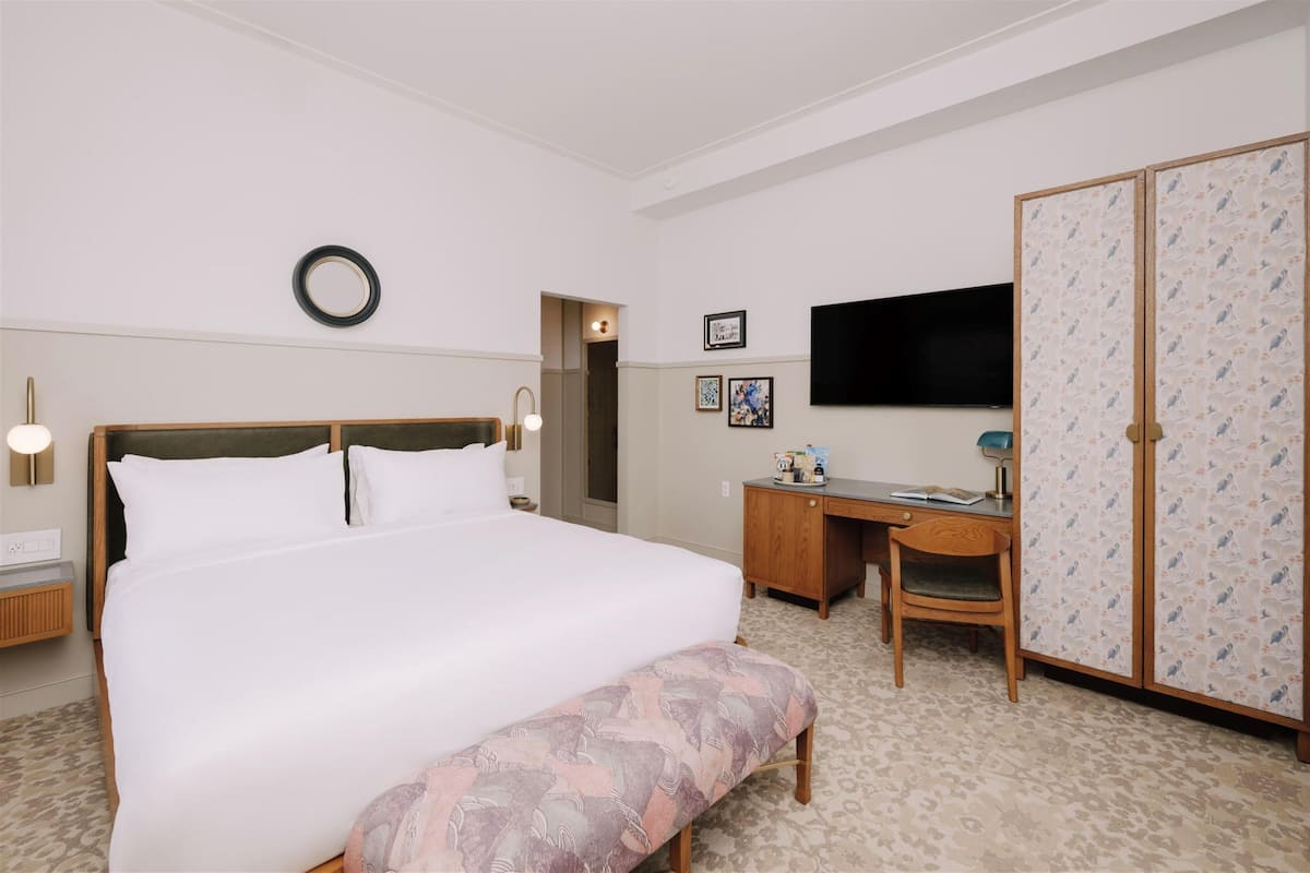 A hotel room with a large bed, a desk, a chair, a wardrobe, and a television on the wall.