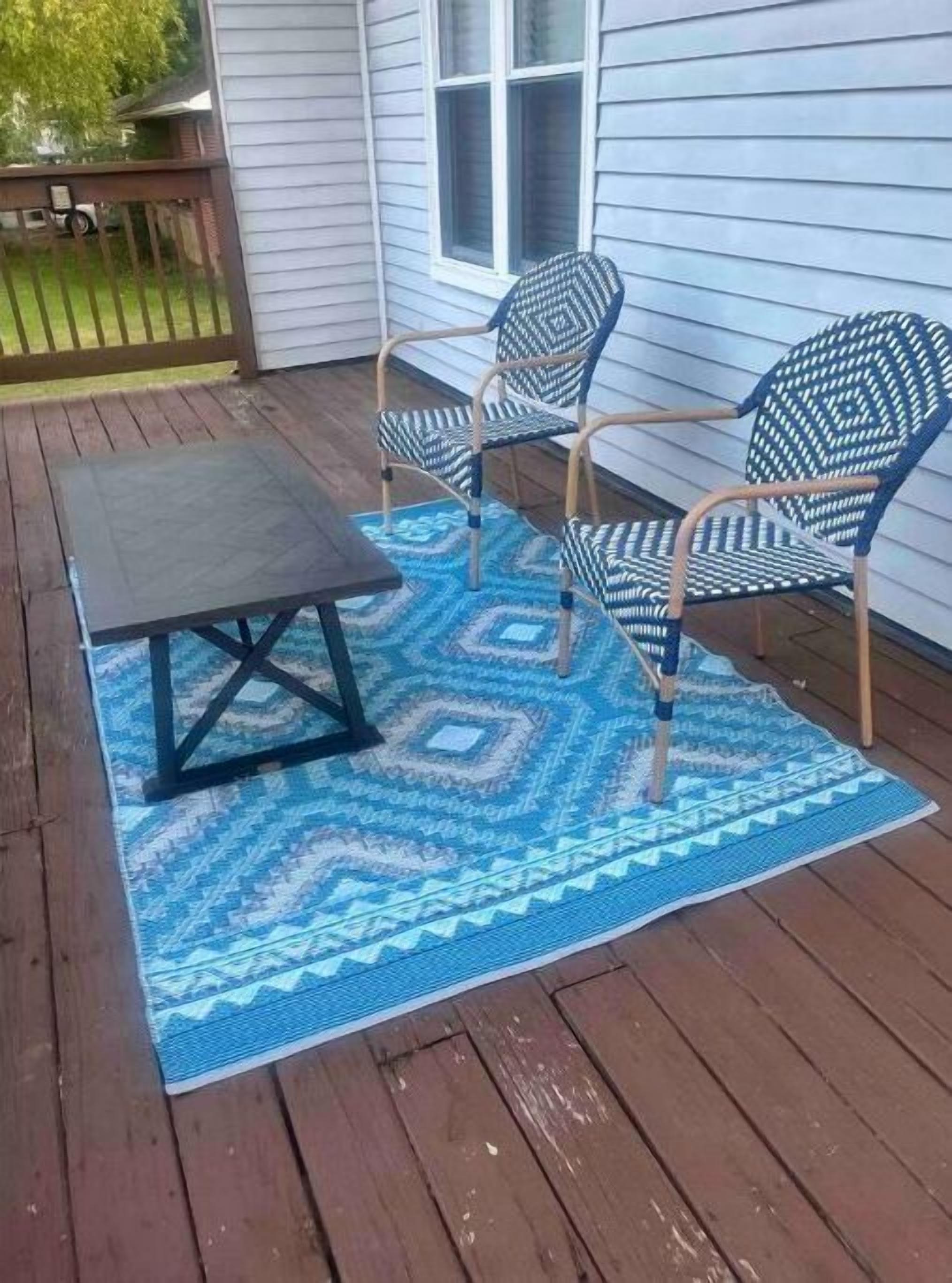 Une terrasse en bois avec une table de pique-nique et deux chaises, un tapis à motifs et une fenêtre avec des stores.