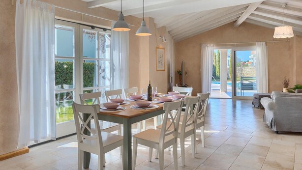 A dining area with a wooden table set for six, white chairs, and pendant lights.