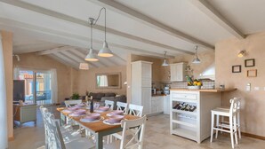 A spacious living area with a dining table set for six, a kitchen with white cabinets, and a balcony with a view.
