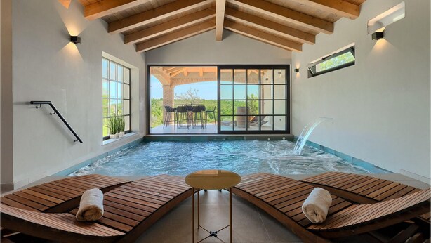 Un espace spa comprenant un bain à remous, des chaises longues en bois et une vue sur l’extérieur.