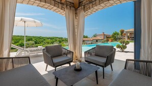 Un espace extérieur aménagé, abrité et doté de deux chaises et d’une table, offrant une vue sur une piscine et une villa.