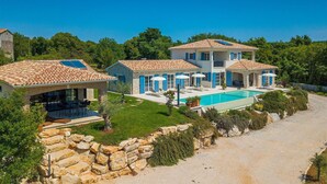 Une maison à deux étages avec une piscine, des murs en pierre et un ciel d’un bleu éclatant.