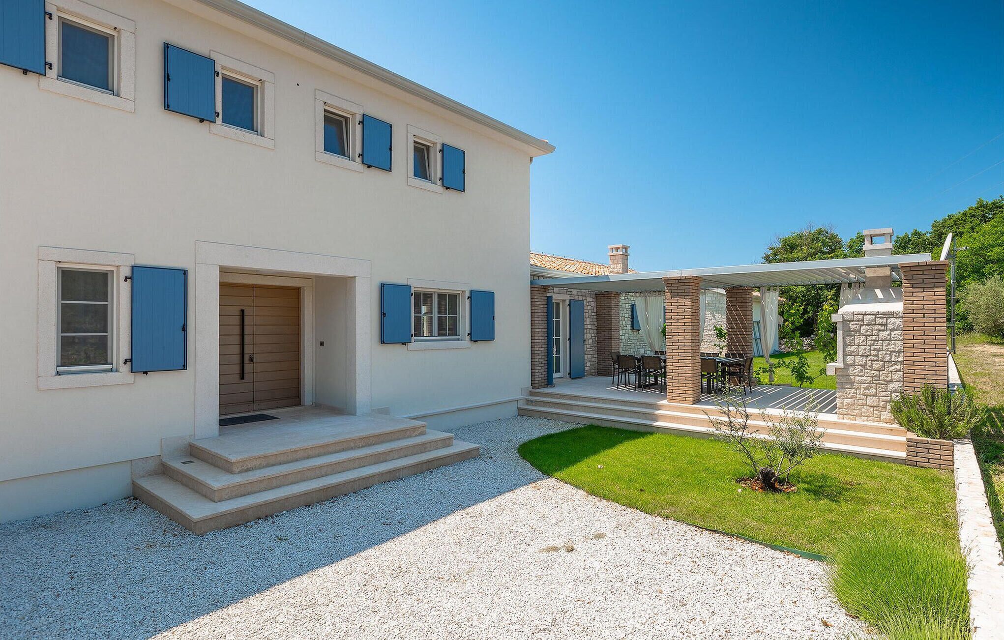 Ein zweistöckiges Haus mit überdachter Terrasse und kleinem Garten.