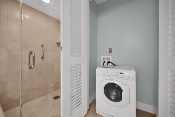 A laundry room with a front-loading washing machine, a glass shower enclosure, and a white door. - Key Bisyne Suite - Steps to sandy Beaches (Key Biscayne)