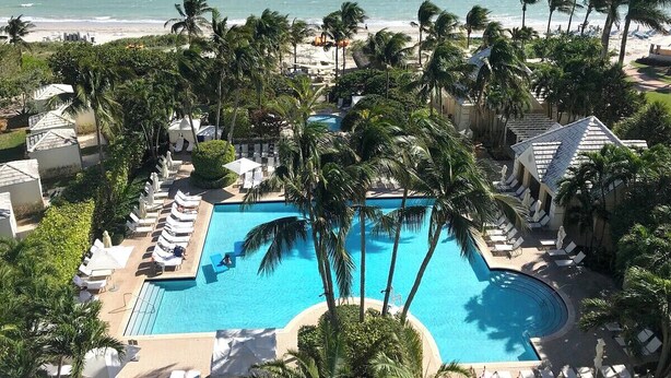 Un complexe hôtelier doté d’une grande piscine entourée de palmiers et de chaises longues, avec vue sur une plage.