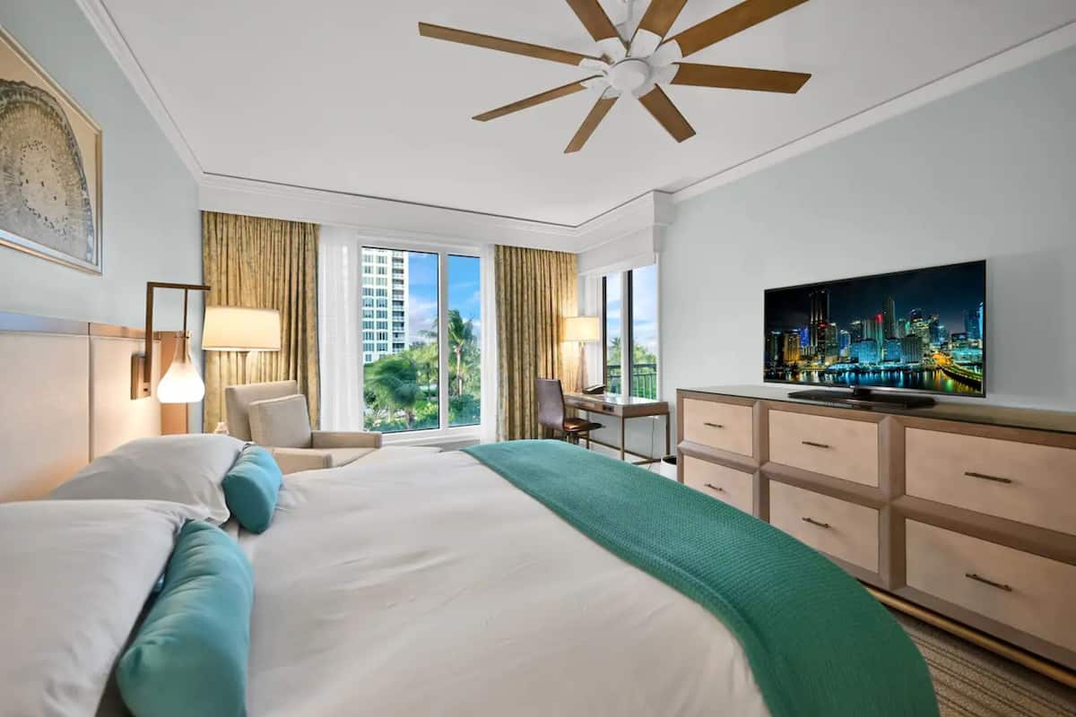 Habitación de hotel con una cama grande, un escritorio, una silla, un televisor y vistas a la ciudad.