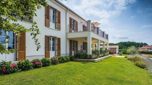 Ein zweistöckiges Haus mit einer Veranda, einem gepflegten Rasen und einem Garten mit rosa Blumen.