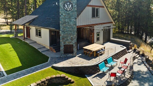 A two-story house with a stone chimney, a patio with outdoor furniture, and a well-maintained lawn.