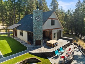 Una casa de dos pisos con una chimenea de piedra, un patio con mobiliario exterior y un césped bien cuidado.