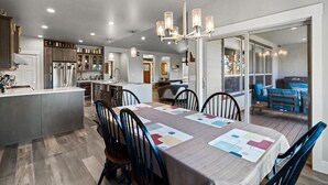A modern kitchen with a central island, dining area with a table and chairs, and a view into a living room with a sofa and a coffee table.