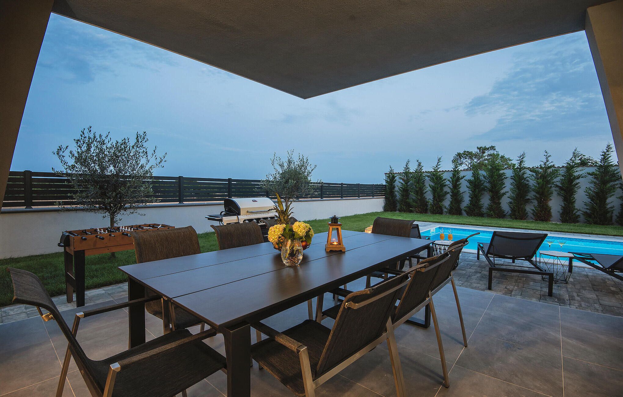 An outdoor patio with a dining table, chairs, a pool, and a grill.