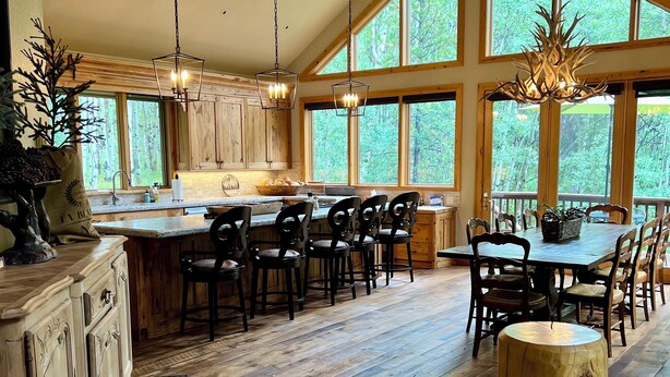 A spacious kitchen with large windows, wooden flooring, and a rustic dining area. - "House in the Forest" Secluded 4BD/3BA luxury home, hot tub, privacy (Crested Butte)