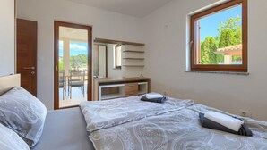 A bedroom with a bed, a desk, a chair, a wardrobe, and a window with a view of greenery. - Beautiful home in Marcana (Marcana)