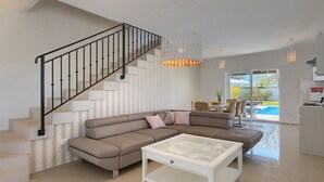 A modern living room with a sectional sofa, a glass coffee table, a staircase with black railings, and a view of a swimming pool through glass doors. - Stunning home in Sveti Petar u Sumi (Sveti Petar u Sumi)