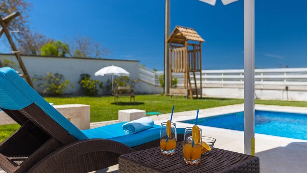 A poolside area with lounge chairs, a table with drinks, and a view of a pool and a wooden structure in the background. - Stunning home in Sveti Petar u Sumi (Sveti Petar u Sumi)