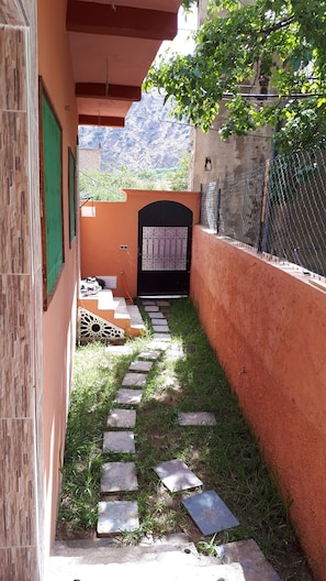Pathway leads to a gated entrance with a building featuring a tiled exterior and a green door.