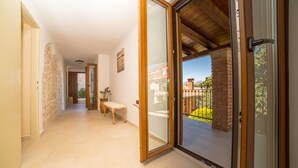 A hallway with a wooden bench, a potted plant, and a sliding glass door leading to an outdoor area with a brick wall and a metal fence.