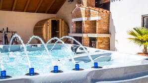 A hot tub with multiple jets, a brick fireplace, and a wooden pergola.