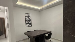 A dining area with a marble table, black chairs, a ceiling light, and a wall-mounted artwork. - JRE Cozy Home Near All Services 19 (Amman)