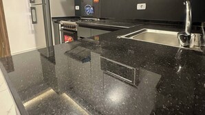 A modern kitchen with a black granite countertop, stainless steel appliances, and a 'SAFE' fire extinguisher. - JRE Cozy Home Near All Services 19 (Amman)
