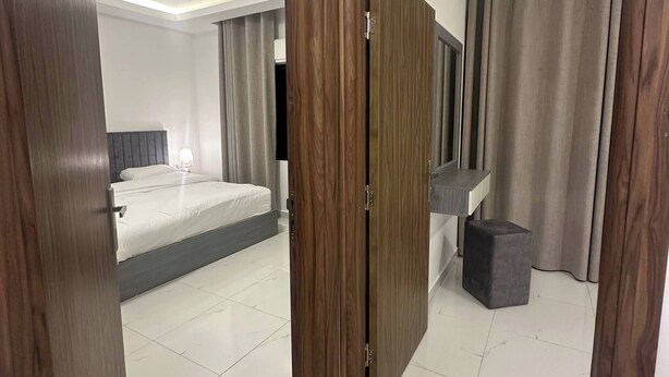 A modern bedroom with a bed, a bedside table, a mirror, and a wardrobe. - JRE Cozy Home Near All Services 19 (Amman)