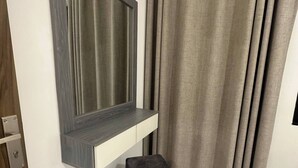 A modern room with a built-in TV shelf, a small grey ottoman, and a window with curtains. - JRE Cozy Home Near All Services 19 (Amman)
