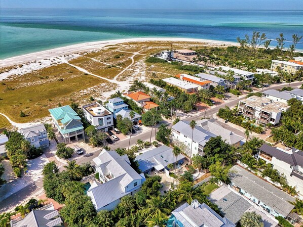 An aerial view of a coastal residential area with houses, a beach, and a clear view of the ocean.