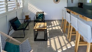 Una stanza luminosa e soleggiata con soffitto alto, zona pranzo con bancone e angolo salotto con sedie e tavolo.