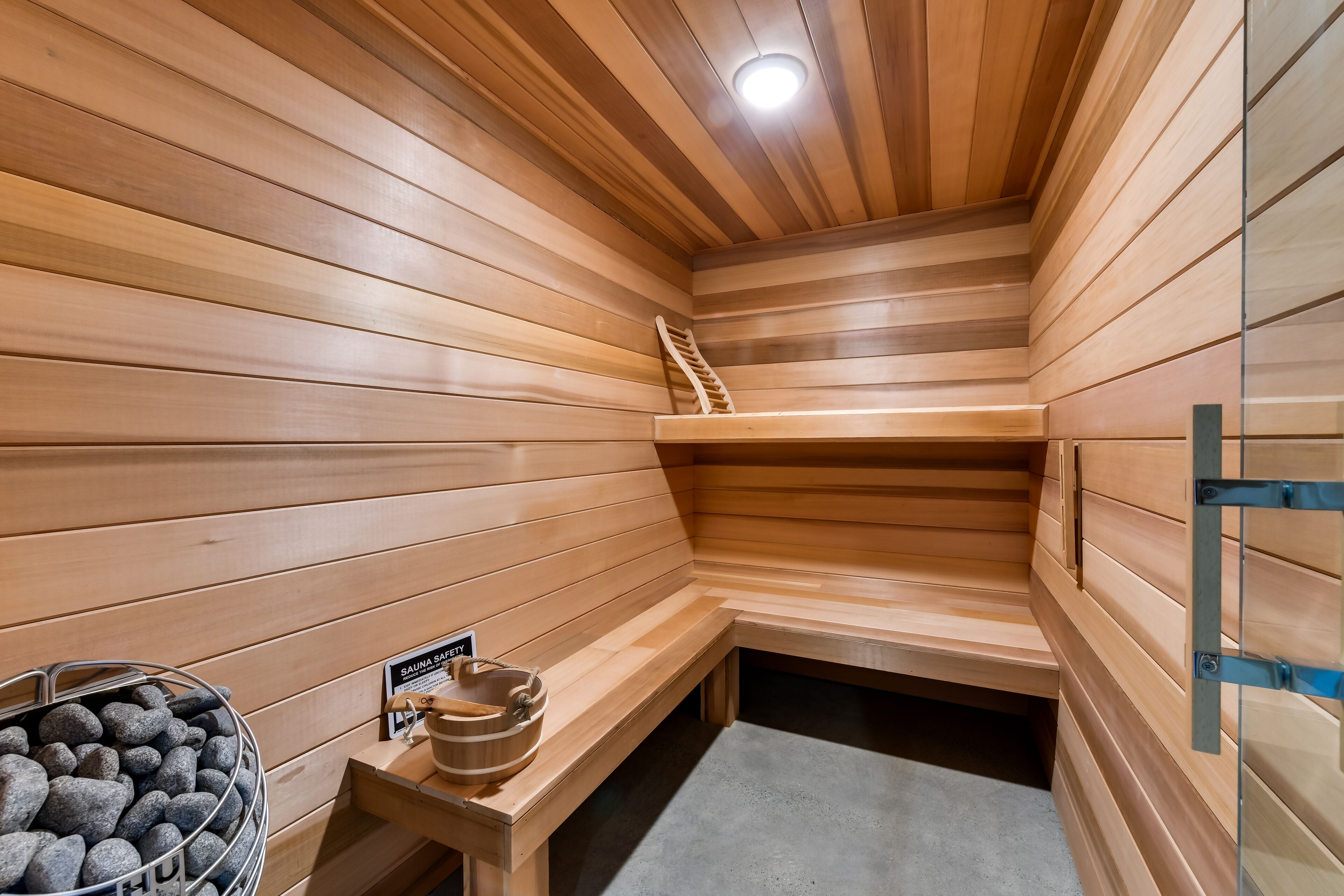 A sauna room with wooden walls and benches, a stone basin with a sign, and a wooden ladder.