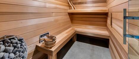 A sauna room with wooden walls and benches, a stone basin with a sign, and a wooden ladder.