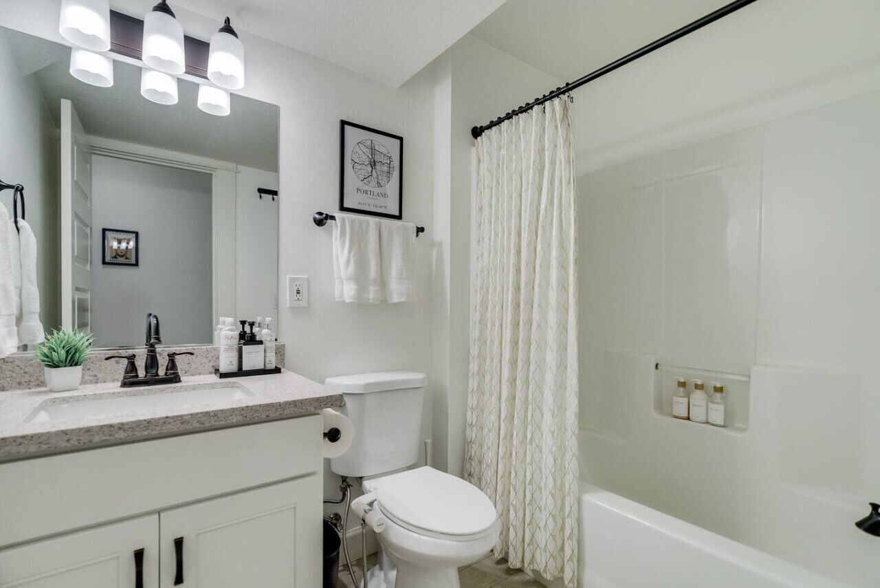 A bathroom with a toilet, sink, and bathtub. There is a shower curtain, a mirror, and a framed picture on the wall.