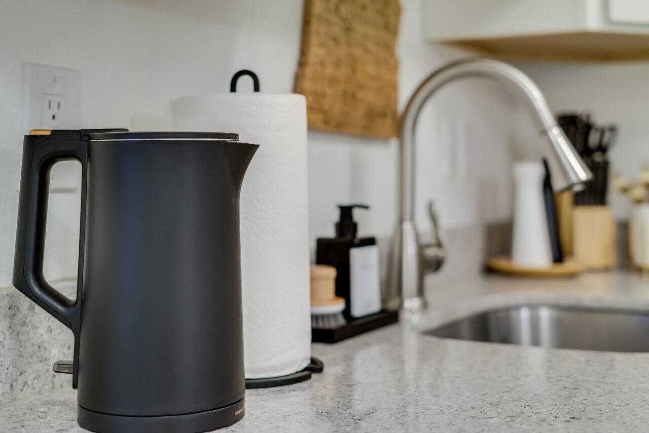 Une cuisine équipée d’une bouilloire électrique noire, d’un rouleau d’essuie-tout et d’un évier en acier inoxydable.
