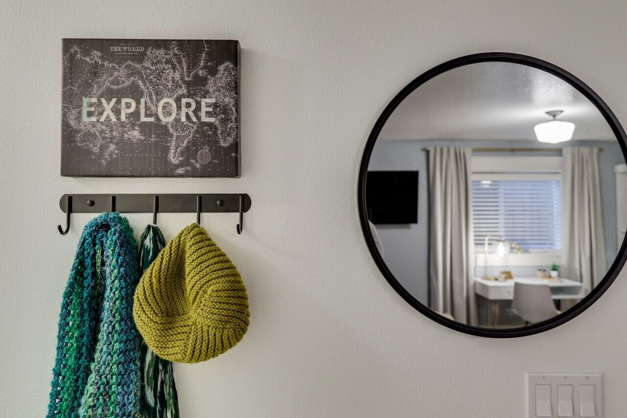Een spiegel aan de muur die een kamer weerspiegelt met een bureau en een raam.