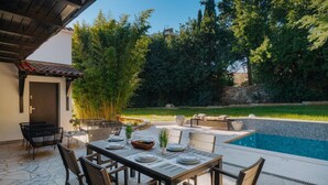 Un espace extérieur aménagé pour les repas, avec une piscine, entouré de verdure et délimité par un mur de pierres.