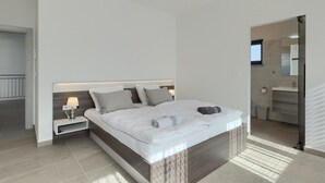 A modern bedroom with a large bed, bedside tables with lamps, a built-in wardrobe, and a bathroom with a mirror and sink. - Amazing home in Porec (Porec)