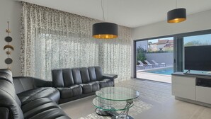 A modern living room with a leather sofa, a glass coffee table, and a view of a swimming pool through large windows. - Amazing home in Porec (Porec)