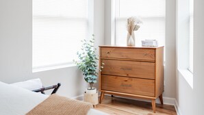A bedroom with a wooden dresser, a bedside plant, and a window with blinds. - Duplex 2 Bedroom and 1.5 Bath Retreat Near Loyola Park (Chicago)