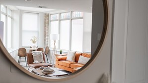 A living room with a round mirror reflecting the space, a sofa, a coffee table, and a dining area with chairs and a table. - Duplex 2 Bedroom and 1.5 Bath Retreat Near Loyola Park (Chicago)