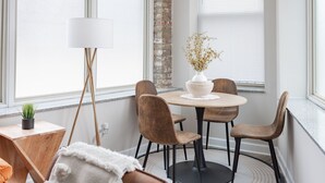 A dining area with a round table, four chairs, a vase with dried flowers, a floor lamp, and a brick wall. - Duplex 2 Bedroom and 1.5 Bath Retreat Near Loyola Park (Chicago)