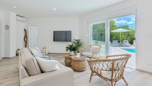 A modern living room with a sofa, wicker chairs, a TV, and a view of a pool and garden. - Cozy home in Drivenik (Drivenik)