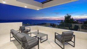 A rooftop terrace with a view of the sea and cityscape at dusk. - Beach front home in Podstrana (Podstrana)