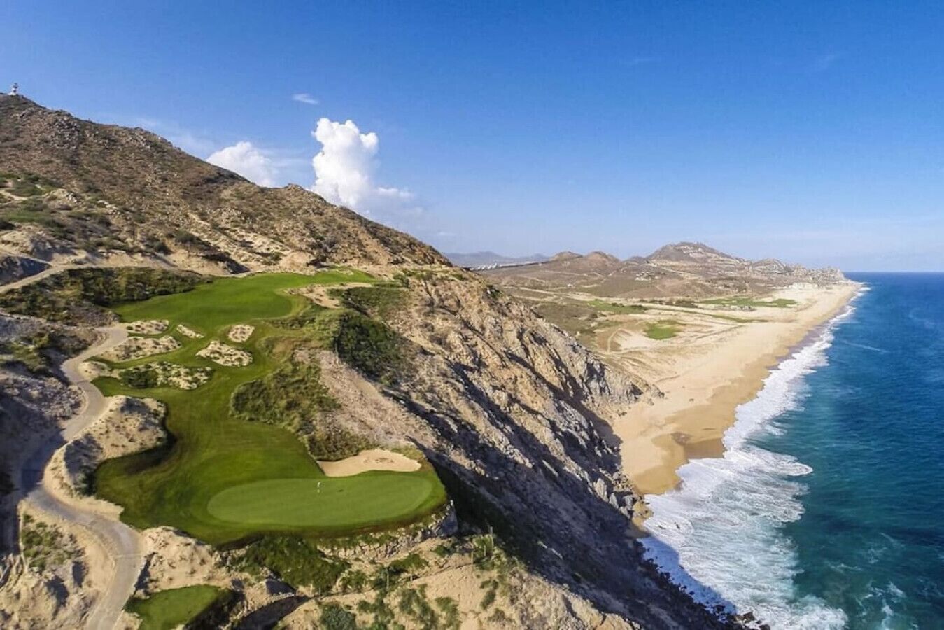 Un campo da golf costiero con spiaggia e terreno roccioso.