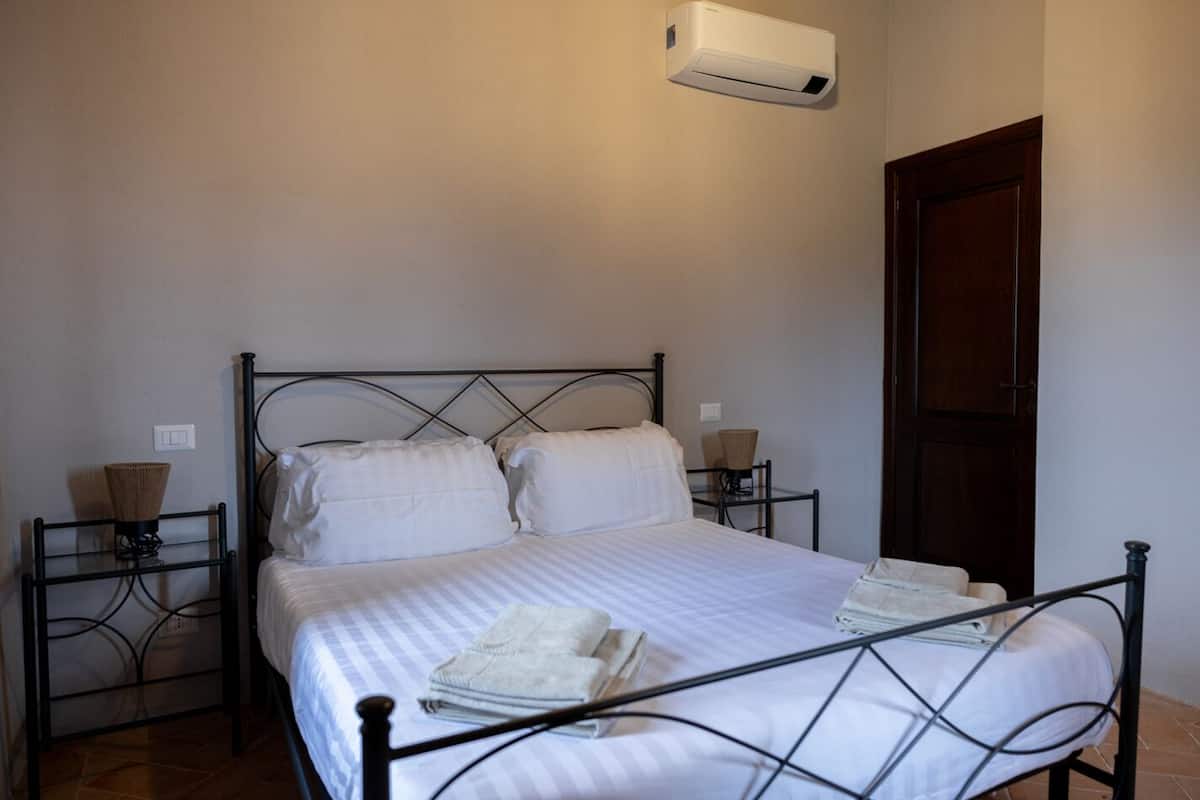 Una cama individual con estructura metálica, ropa de cama blanca y un aire acondicionado instalado en la pared.