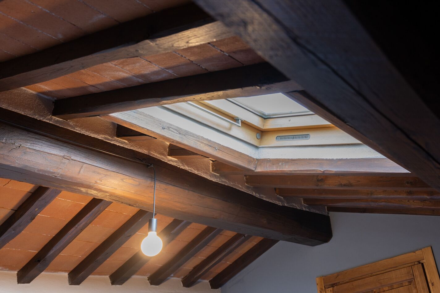 A skylight in a room with exposed wooden beams and a hanging light fixture.