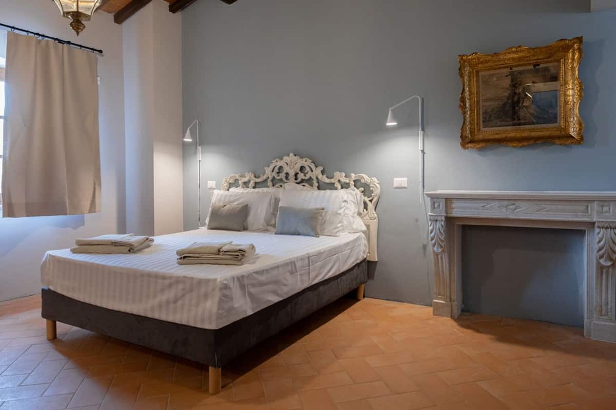 Un dormitorio con una cama, dos lámparas de noche, una chimenea y un cuadro en la pared.