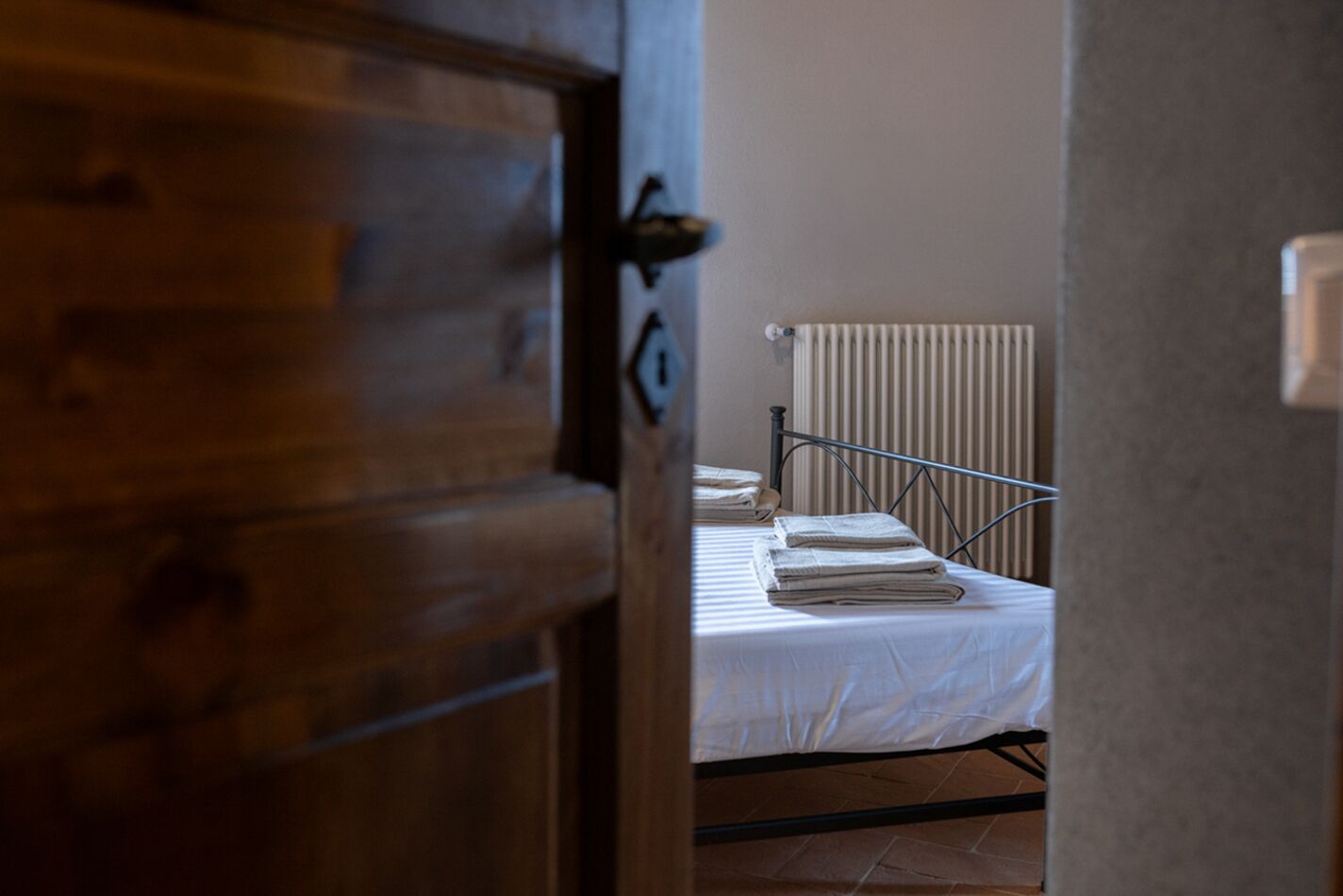 Una habitación con una puerta de madera, una cama con estructura metálica y un radiador.