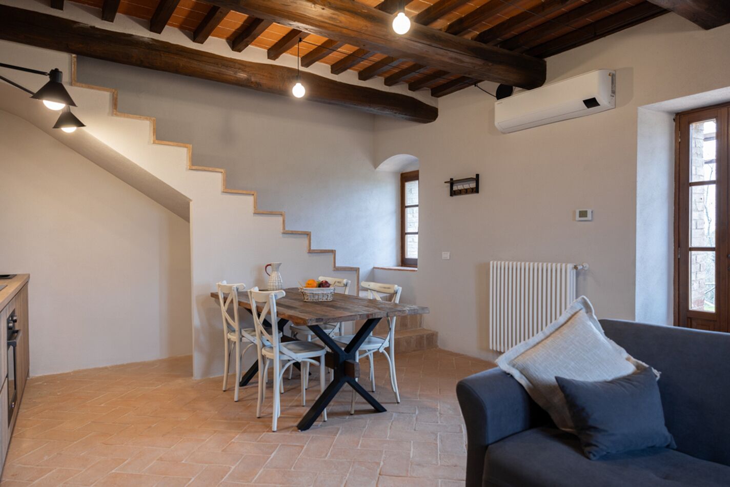 A cozy living area with a dining table, chairs, a sofa, a staircase, and a radiator.
