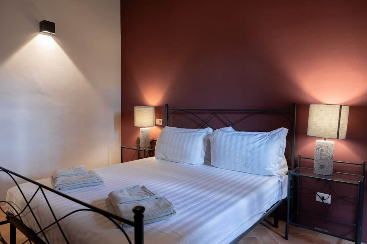 Una cama bien hecha con sábanas blancas, dos lámparas de noche y una toalla doblada sobre la cama.