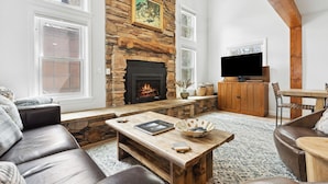 A living room with a stone fireplace, leather sofa, wooden coffee table, and a television. - Downtown, Walk to Main, 1 mile to ski resort (Breckenridge)